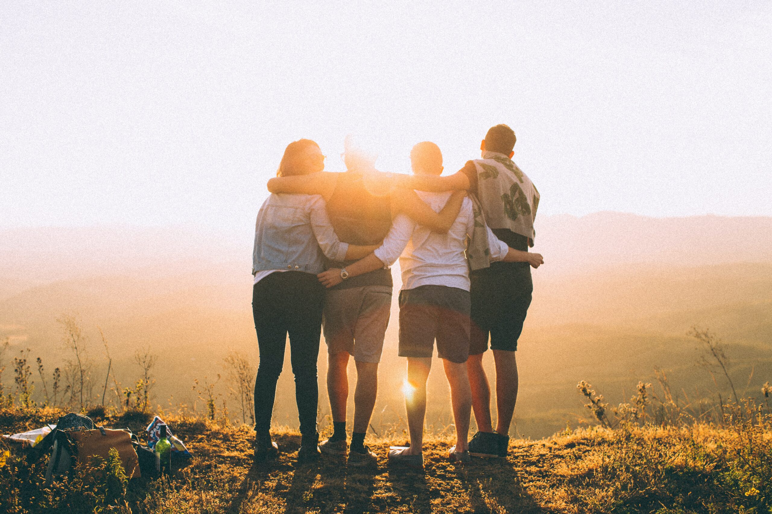 4 people with arms around each other at sunset