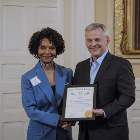 Dr.D and Gov. Josh Stein standing together holding a framed certificate.