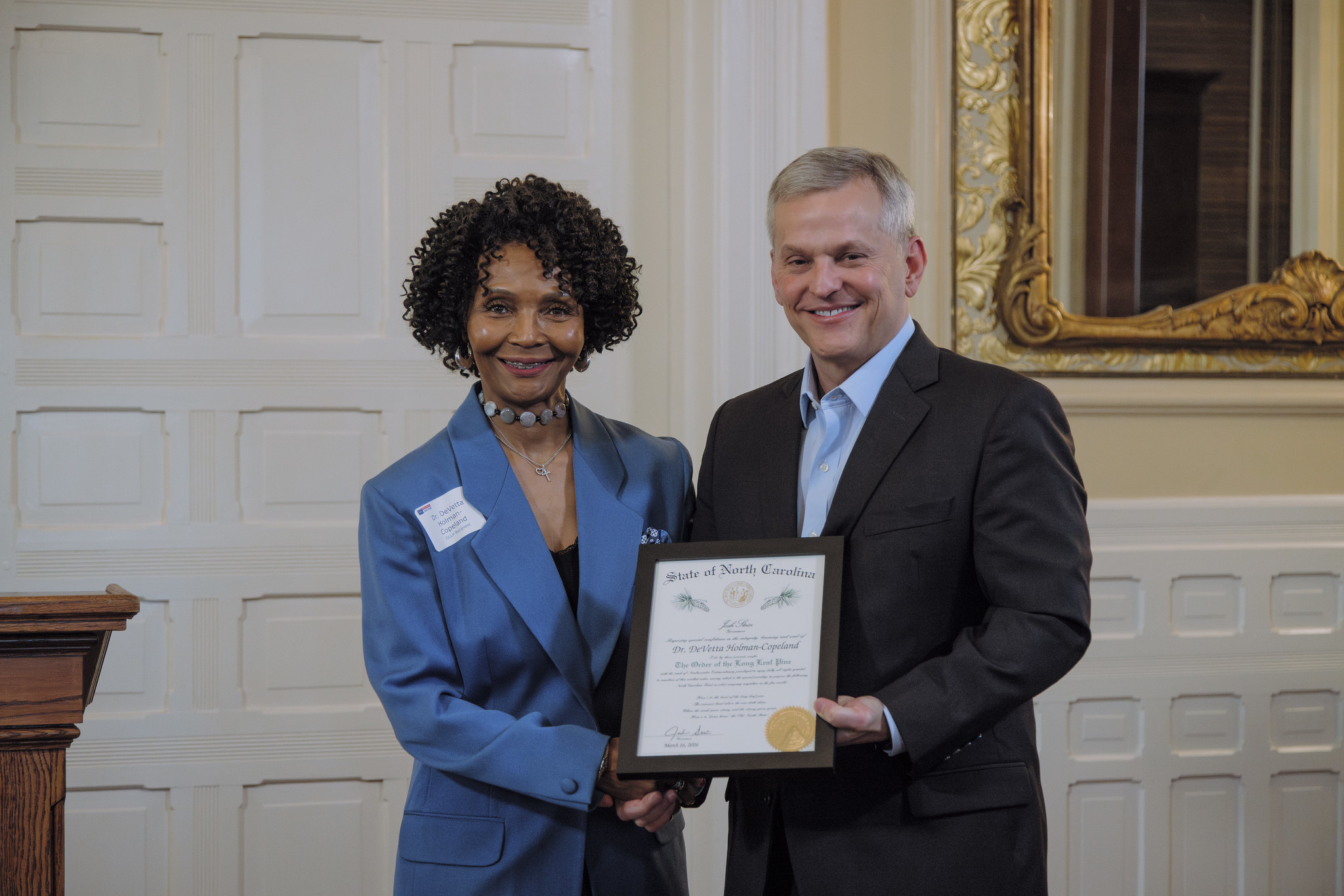 Dr.D and Gov. Josh Stein standing together holding a framed certificate.