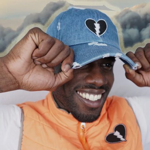 Smiling man tugs on a hat with a Live Black Heart logo on it.